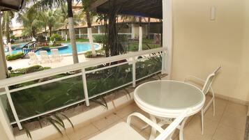 Un balcón con una mesa y sillas de vidrio, con vista a una piscina y palmeras.