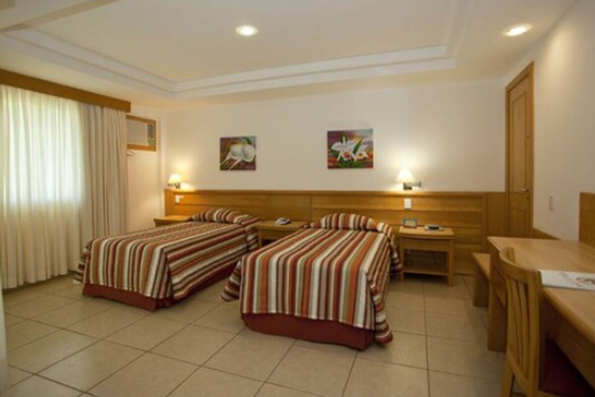Een hotelkamer met twee enkele bedden, een houten bureau, een stoel en twee nachtkastjes.