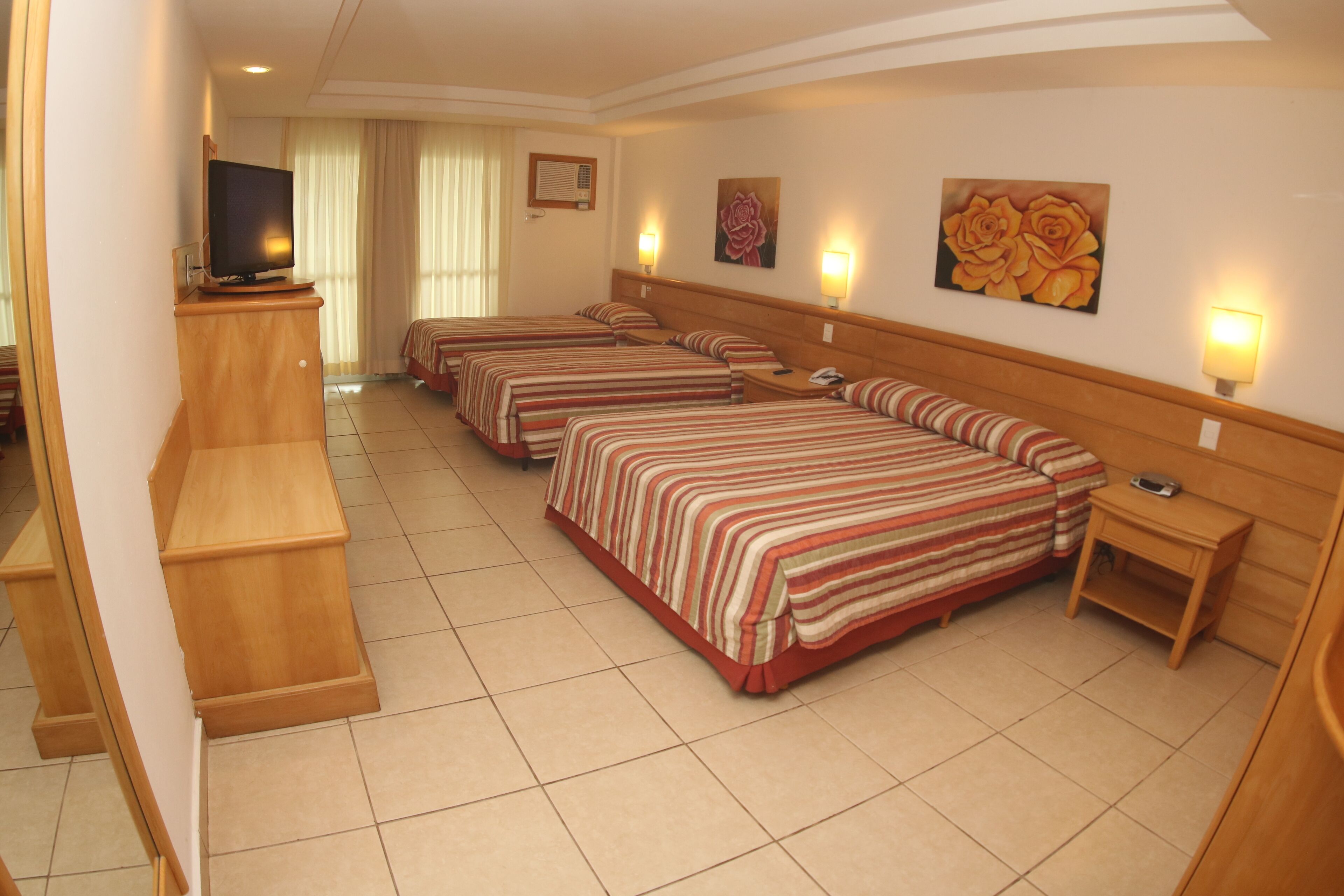 Ein Hotelzimmer mit vier Einzelbetten, einem Fernseher, Nachttischlampen und einem kleinen Schreibtisch.