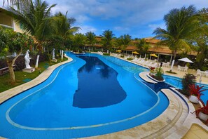 A swimming pool with a curved design, surrounded by palm trees and lounge chairs. - Hotel Atlantico Buzios Convention and Resort (Búzios)