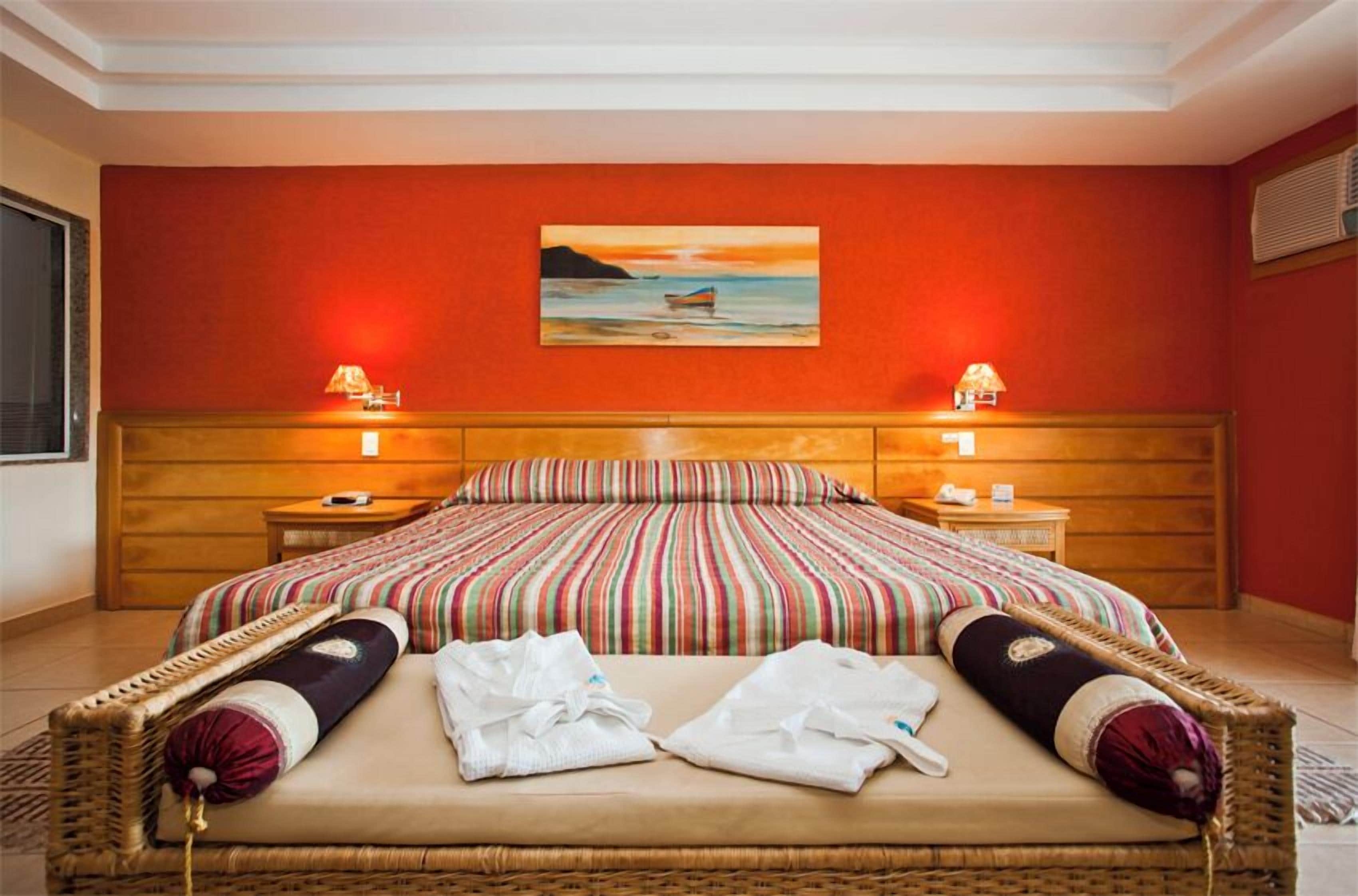 Une chambre d’hôtel avec un grand lit, deux tables de chevet, un tableau représentant un bateau accroché au mur et une fenêtre sur le côté gauche.