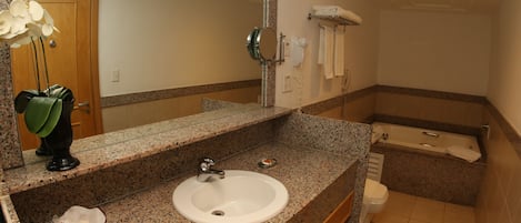 Un baño con lavamanos de encimera de granito, espejo, toallero y bañera.