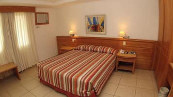 Habitación de hotel con una cama grande, dos mesitas de noche, un escritorio, una silla, una ventana con cortinas y un cuadro en la pared.