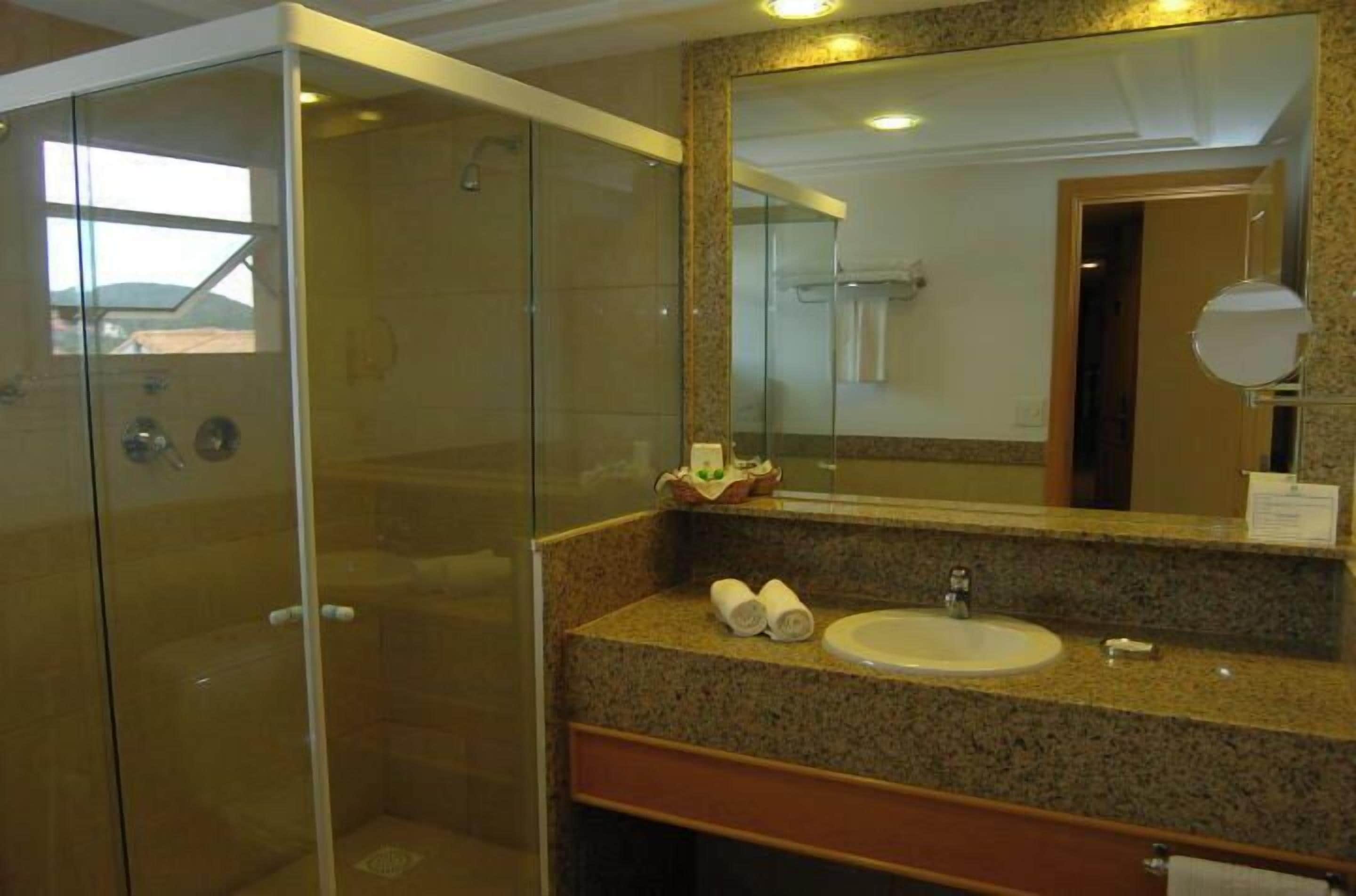 Un baño moderno con ducha envuelta en vidrio, encimera de granito y un espejo grande.