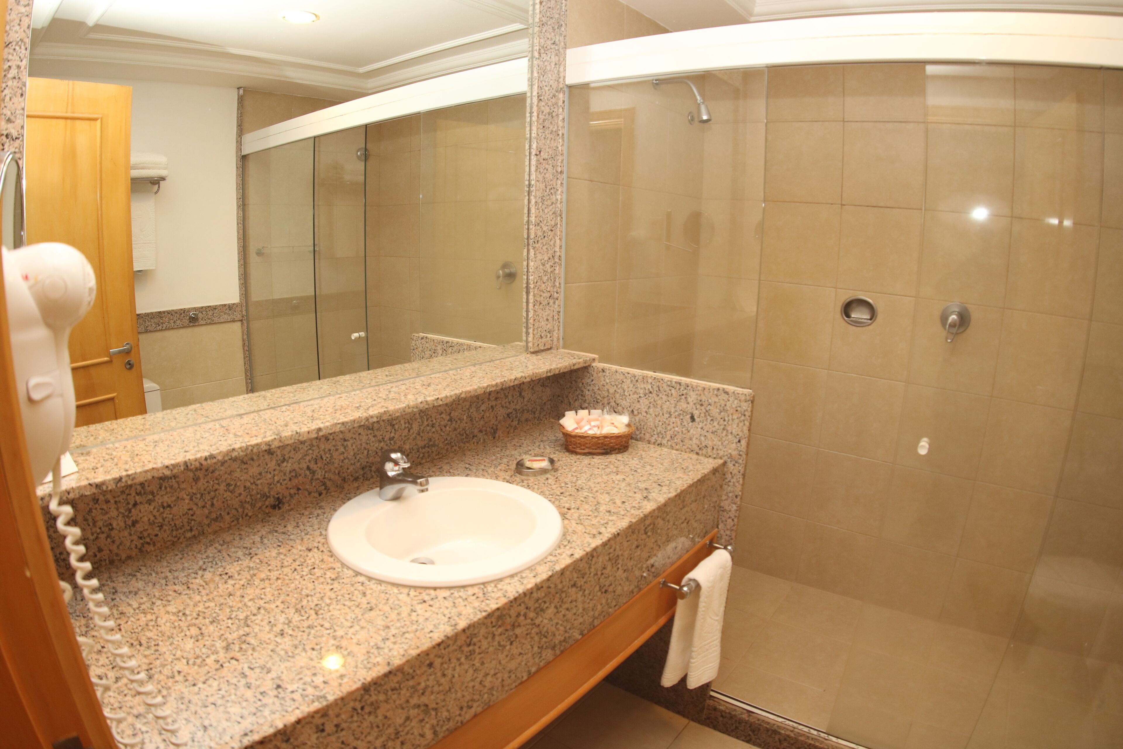 A bathroom with a granite countertop sink, a mirror, a shower with a glass door, and a towel rack.