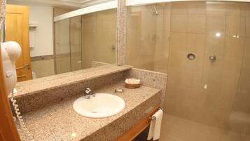 A bathroom with a granite countertop sink, a mirror, a shower with a glass door, and a towel rack.