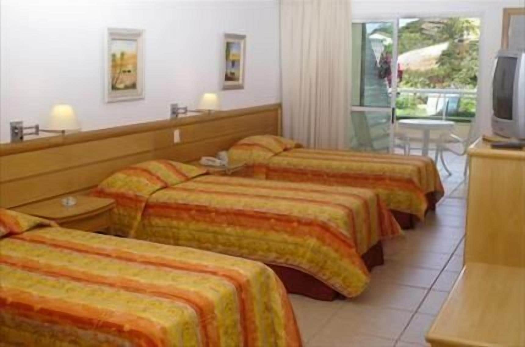 A hotel room with four beds, a TV, and a balcony with a view of the outdoors.