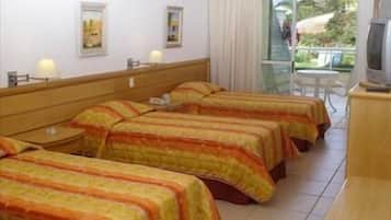 A hotel room with four beds, a TV, and a balcony with a view of the outdoors.