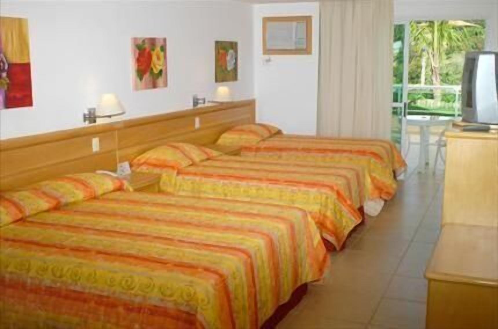 Habitación de hotel con cuatro camas, televisión y vista a palmeras.