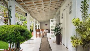 A covered corridor with a tiled floor, potted plants, and a wooden bench.
