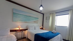 Habitación de hotel con dos camas, un cuadro de una playa, una ventana con cortinas y una luz nocturna.