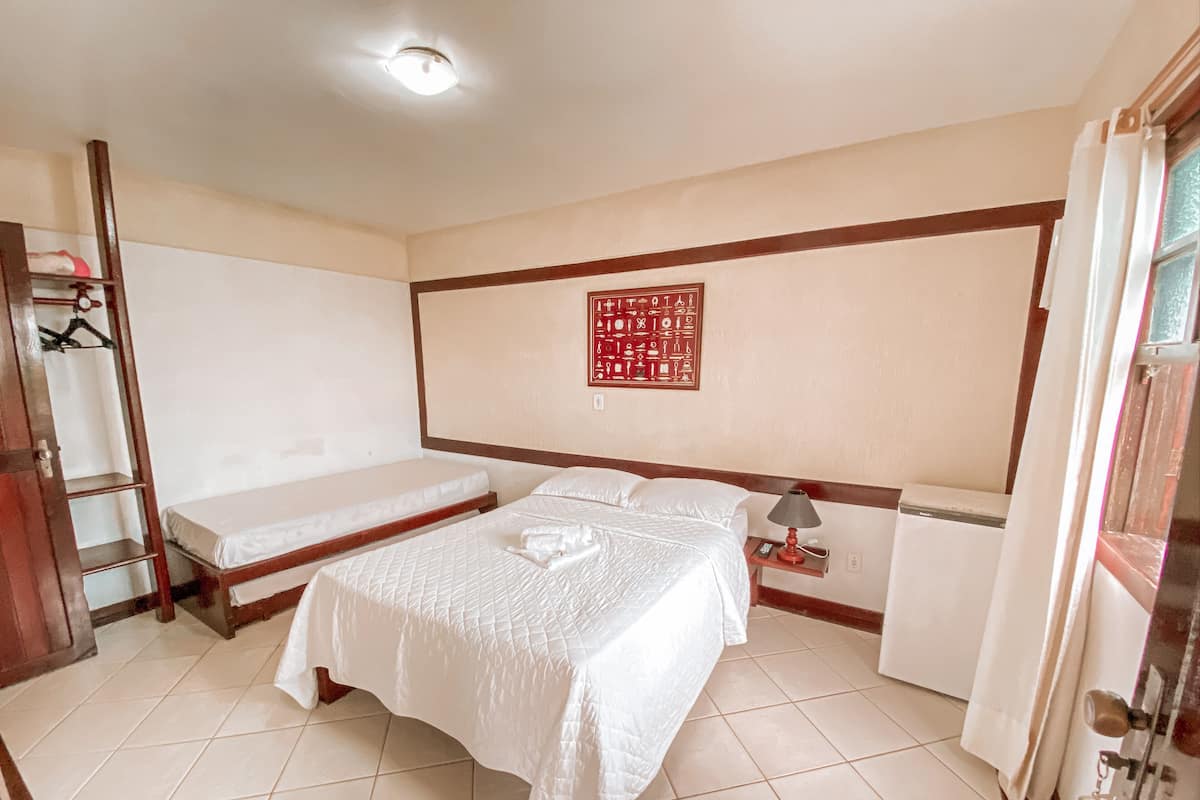 A room with two beds, a wooden wardrobe, a bedside table with a lamp, and a red decorative wall piece.