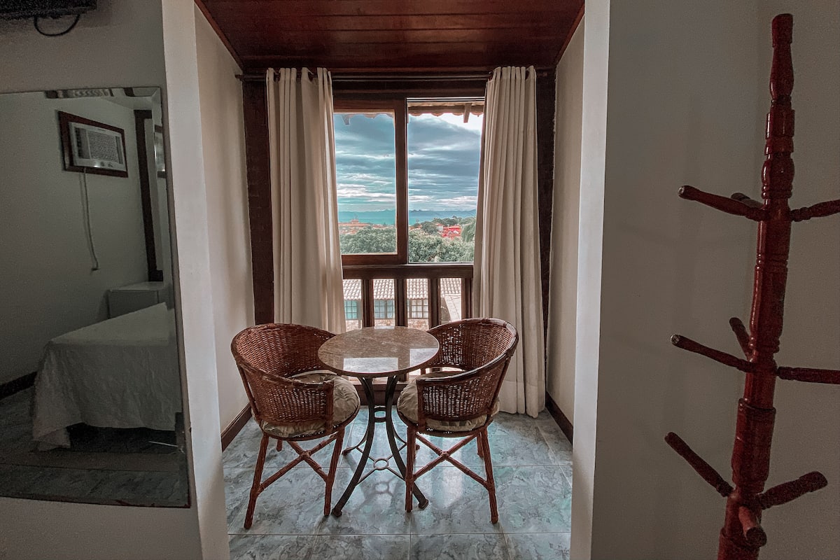A dining area with a table and four wicker chairs, a view of the outdoors, and a wooden ceiling.