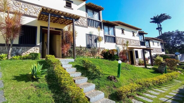Una casa de dos pisos con fachada de piedra, techo de tejas y un jardín bien cuidado con escalones que conducen a la entrada.