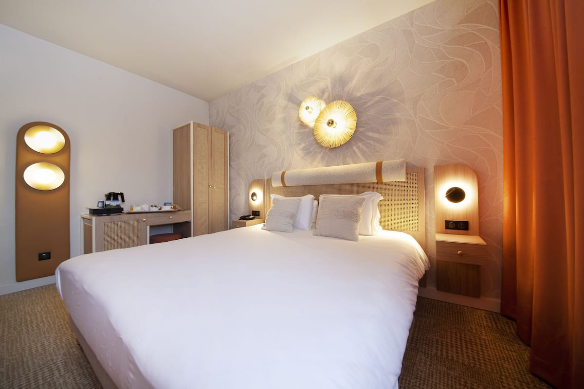 Habitación de hotel con una cama grande, dos mesitas de noche con lámparas, un escritorio con silla y un armario.