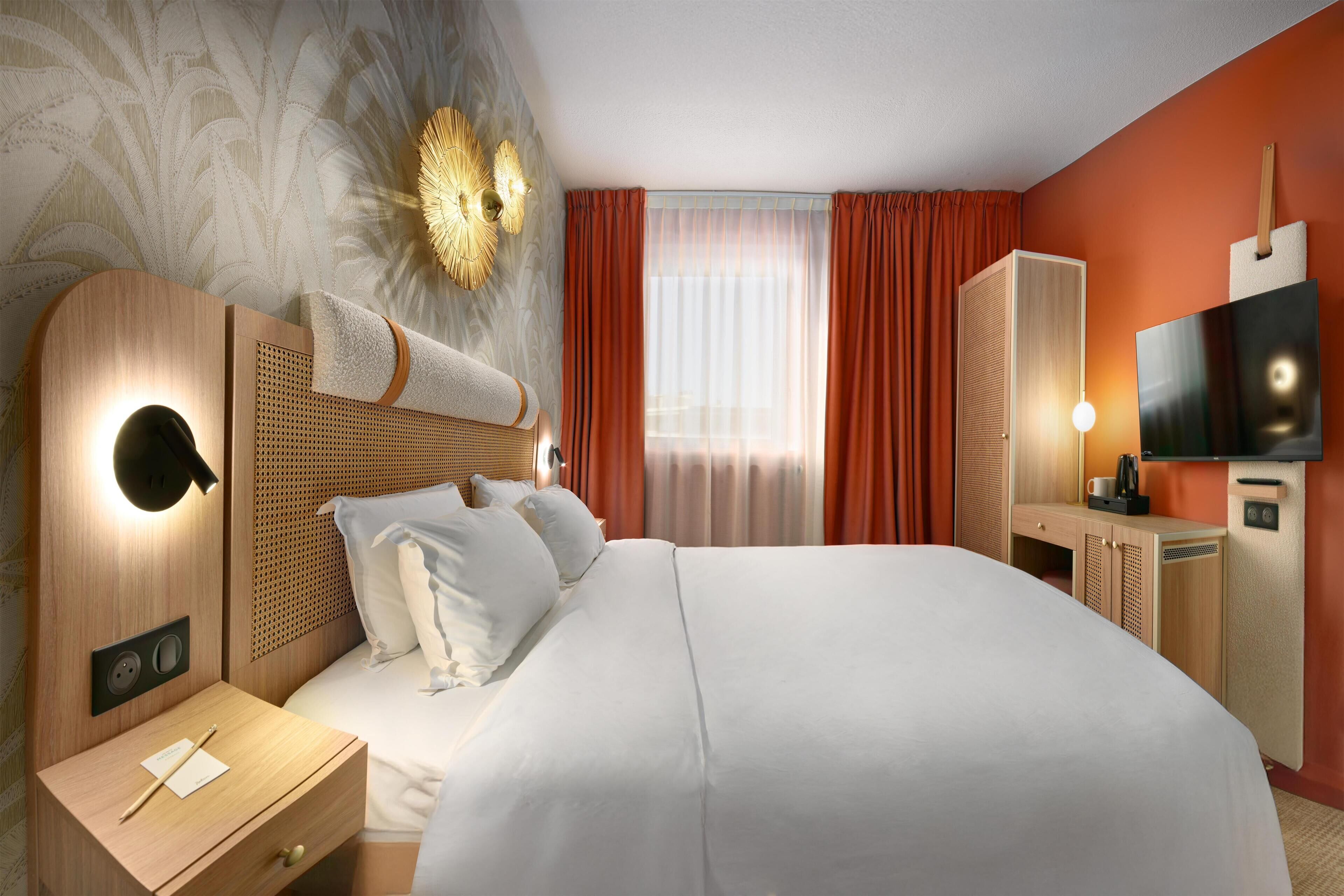 Une chambre d’hôtel moderne dotée d’un grand lit, d’une table de chevet, d’un bureau avec une chaise, d’une armoire, d’un téléviseur à écran plat et d’un appliques murales décoratives.