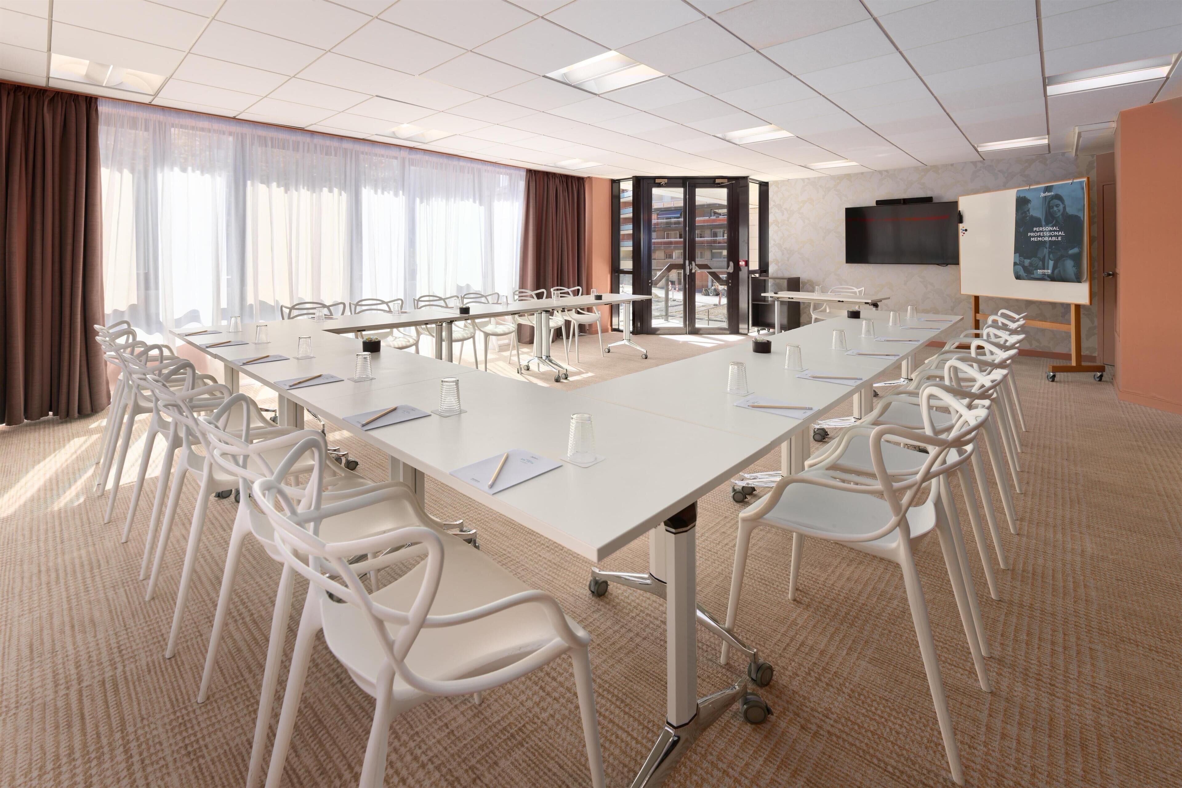 A conference room with a long table, white chairs, and a large screen.
