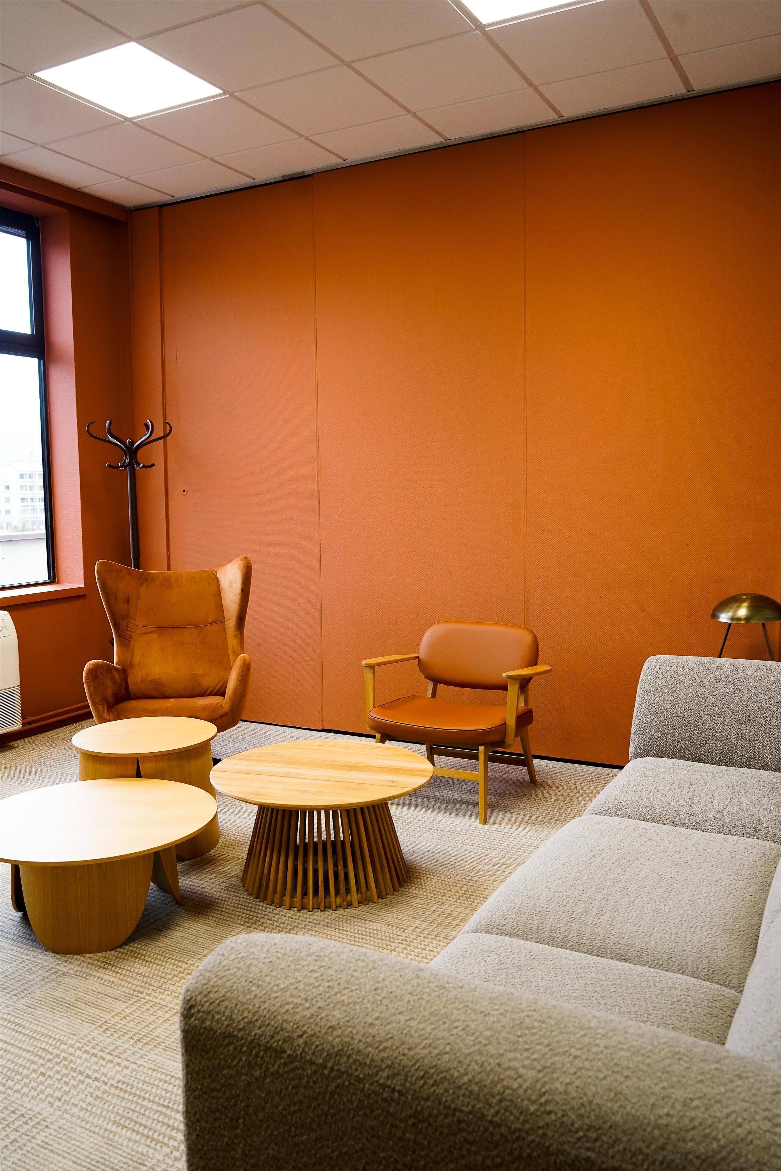 A modern room with orange walls, a large window, and a seating area with a sofa, two armchairs, and a coffee table.