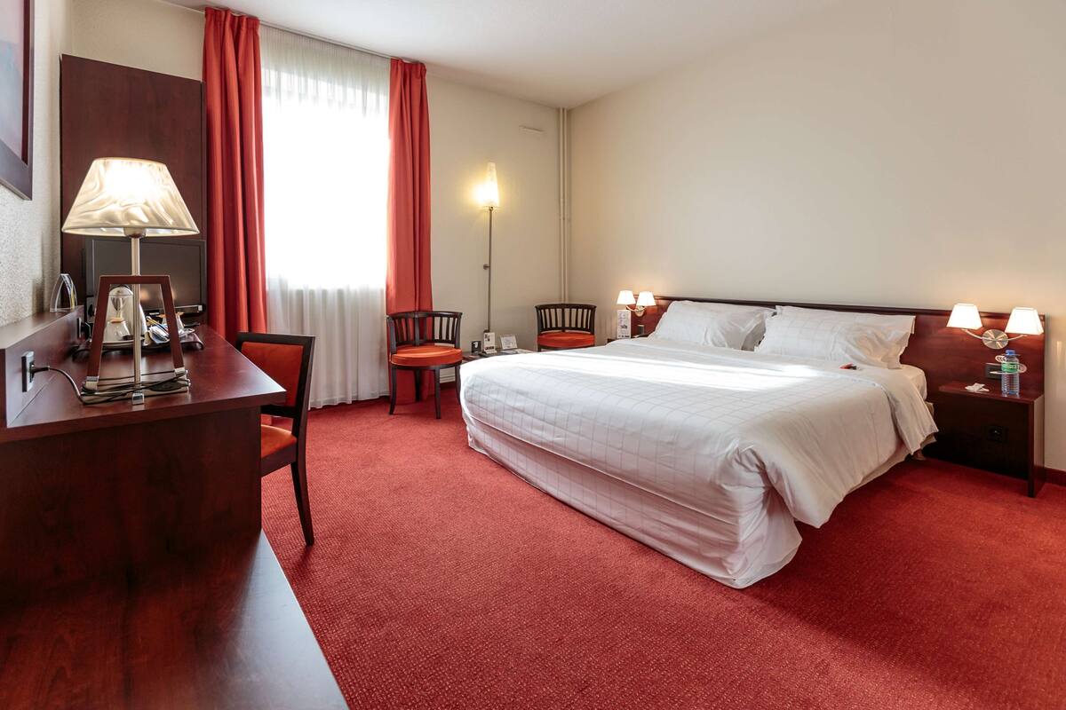 Una habitación de hotel con cama, escritorio, sillas, lámparas y televisor.