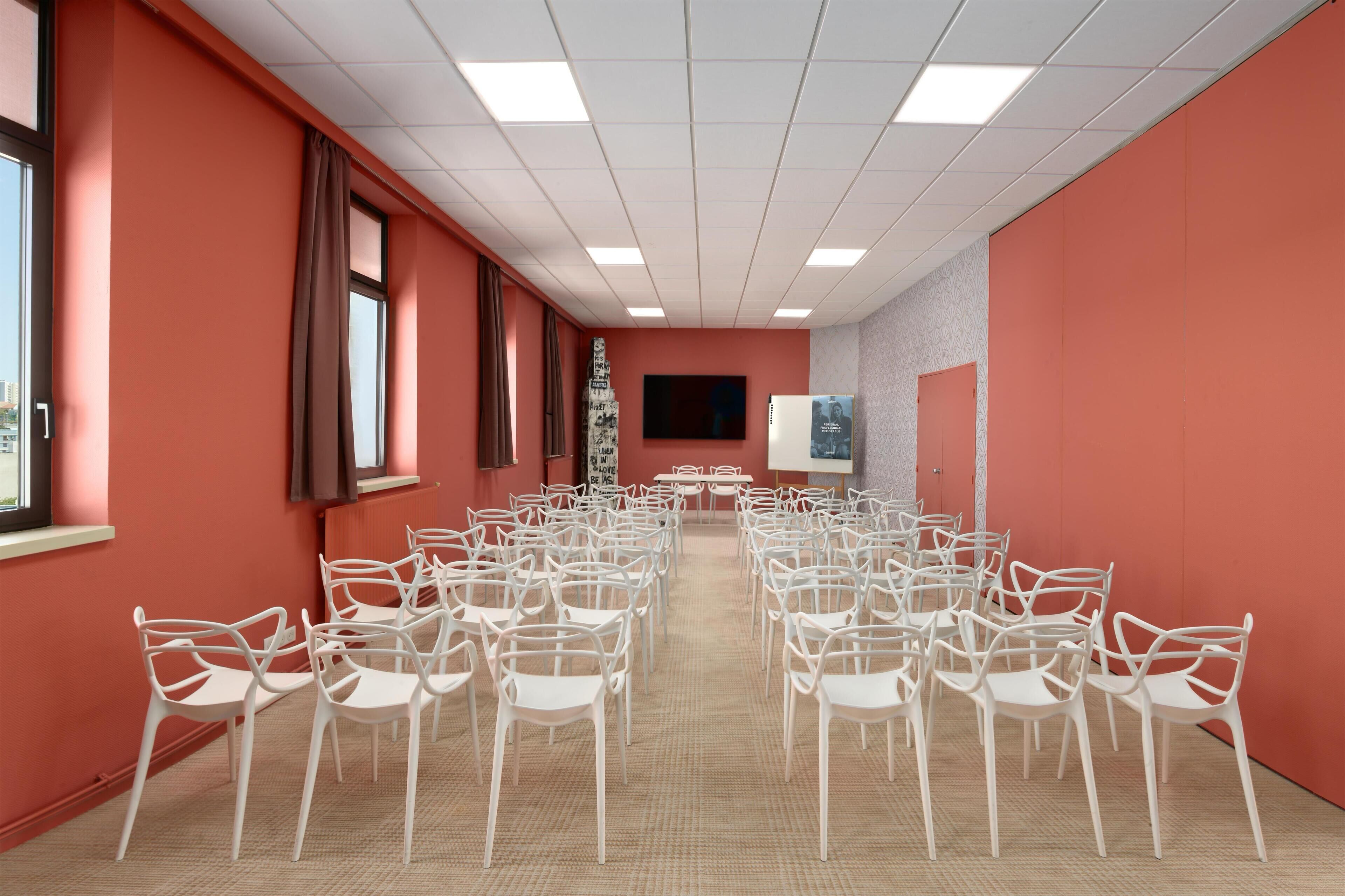 A conference room with rows of white chairs, a large screen, and a projector.