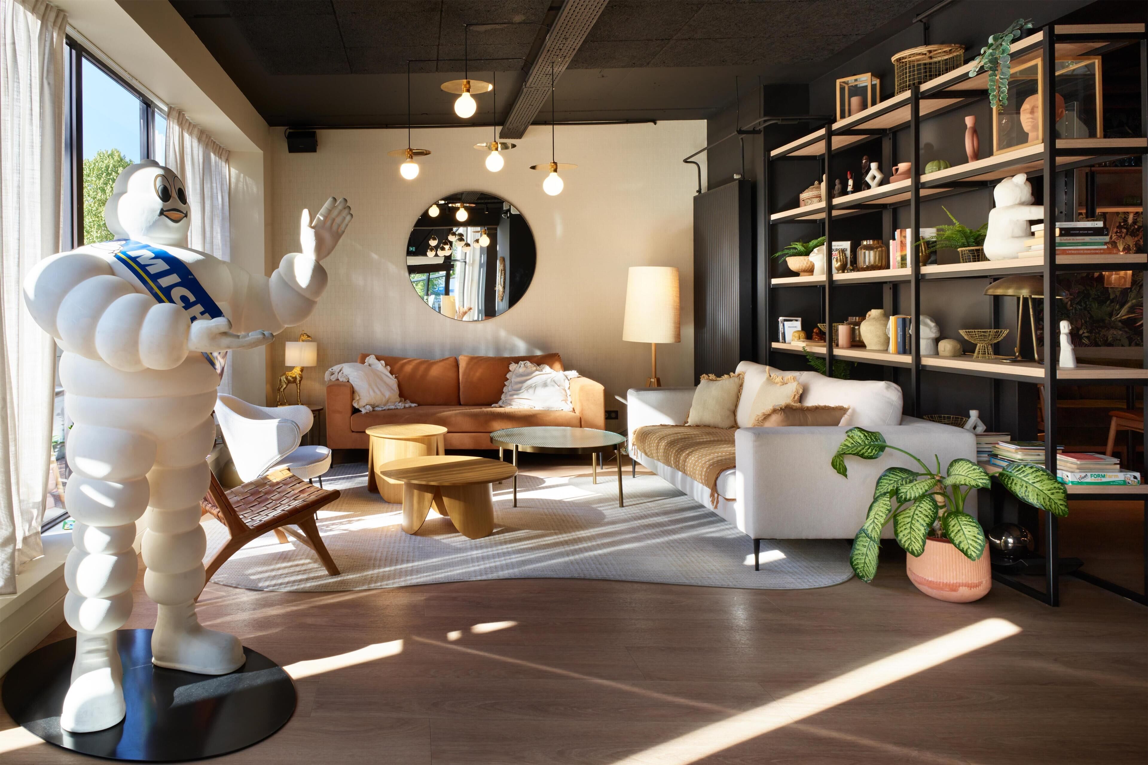 A modern living room with a large white statue, a round mirror, and a bookshelf filled with books and decorative items.