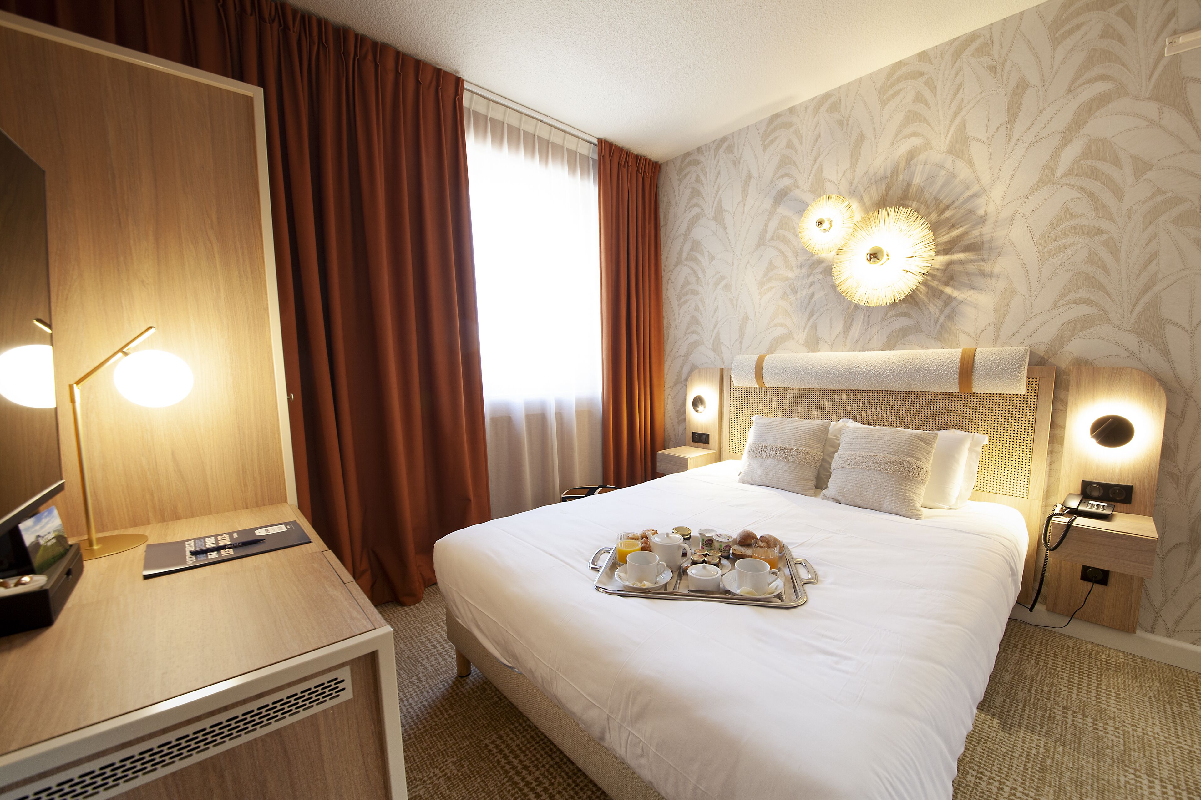 A hotel room with a large bed, a bedside table with a lamp, a tray of breakfast items, and a large mirror.