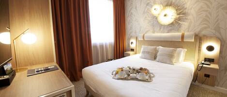 A hotel room with a large bed, a bedside table with a lamp, a tray of breakfast items, and a large mirror.