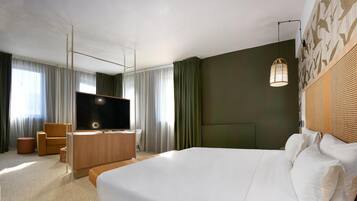 A modern hotel room with a large bed, a flat-screen TV, a wooden desk, and a comfortable armchair.
