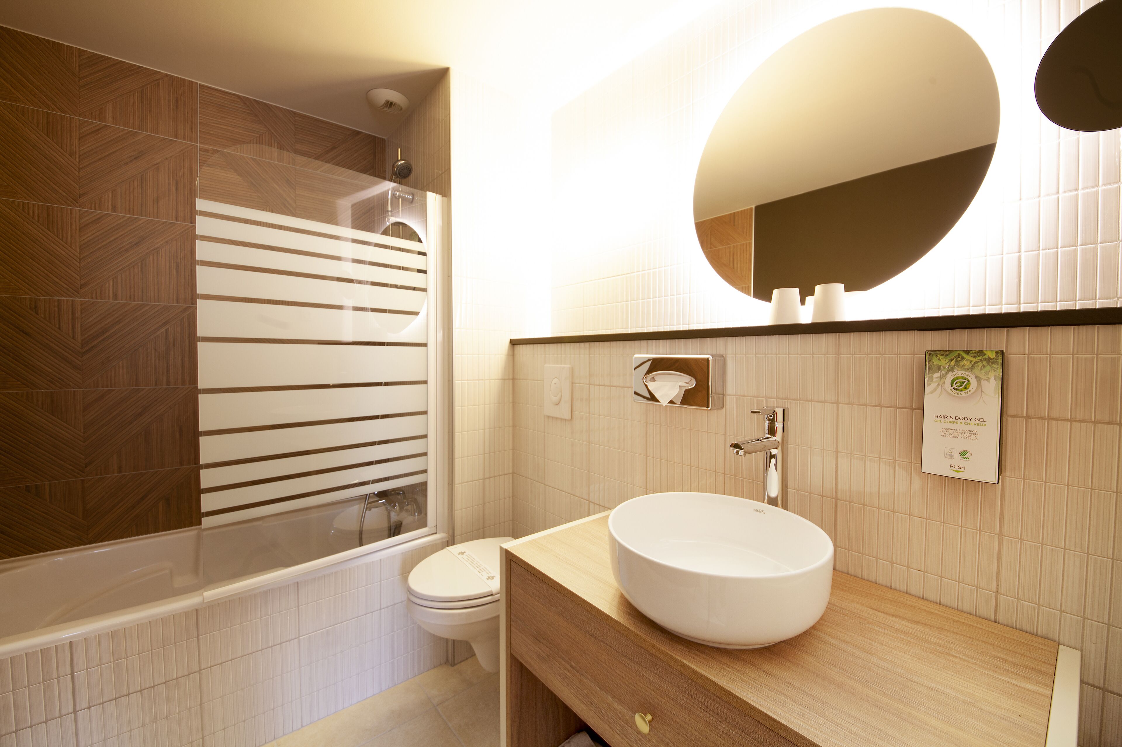 Un baño moderno con un tocador de madera, un espejo redondo grande y un inodoro.
