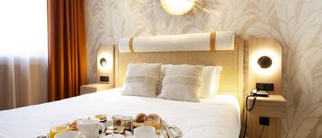 A neatly made bed with a tray of breakfast items, including eggs, toast, and coffee, in a hotel room with patterned wallpaper and a warm light fixture above the bed.