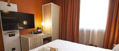 A hotel room with a bed, a TV, a desk with a lamp, and a tray with breakfast items.