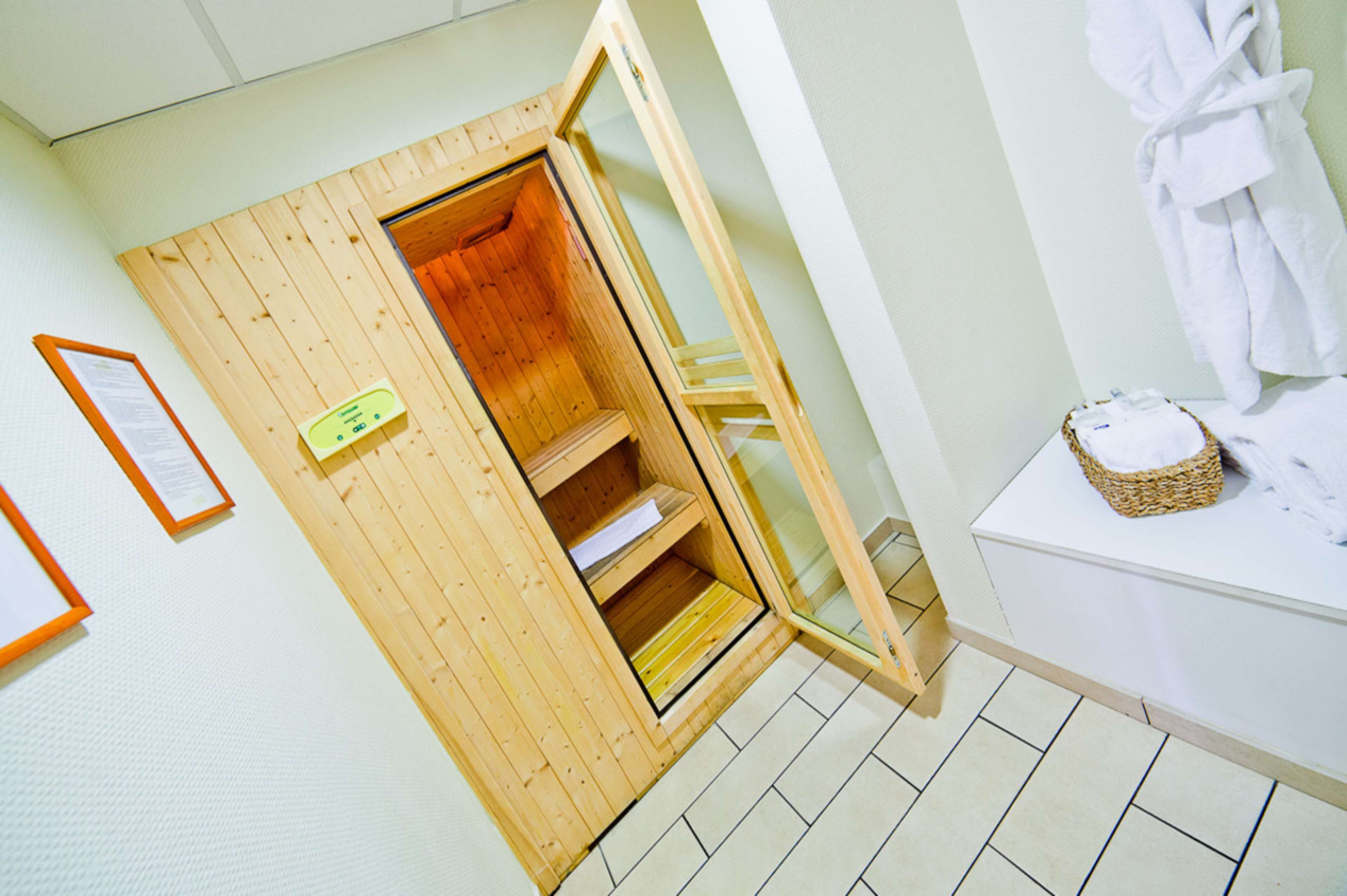 Un cuarto de sauna con paredes de madera y puerta de vidrio, una toalla blanca sobre una encimera y una bata de baño blanca colgada en la pared.