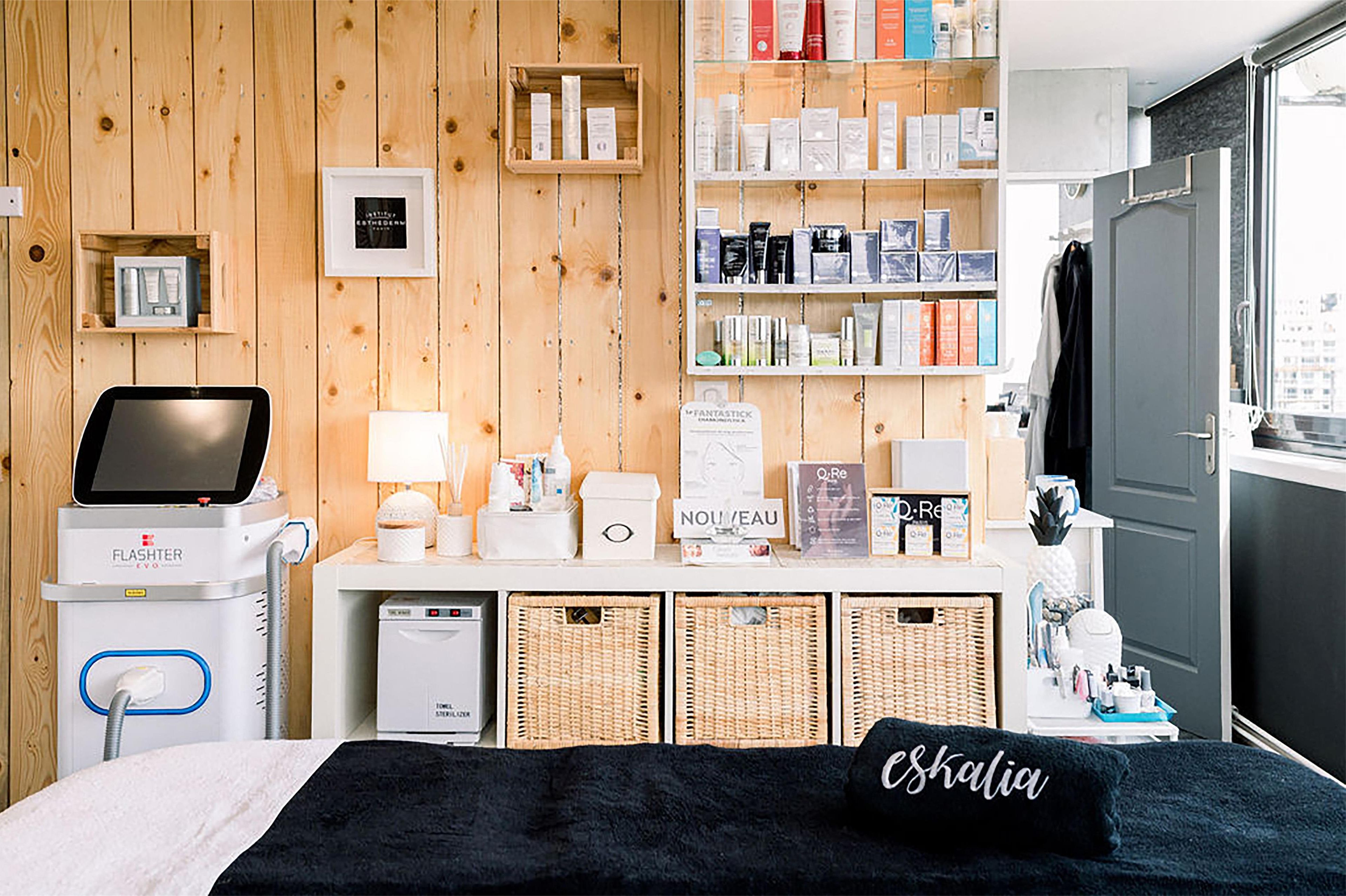 A hotel room with a wooden wall, a bed with a black pillow, a bedside table with a lamp, a hairdryer, and a shelf with toiletries.