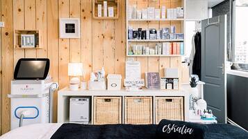 A hotel room with a wooden wall, a bed with a black pillow, a bedside table with a lamp, a hairdryer, and a shelf with toiletries.