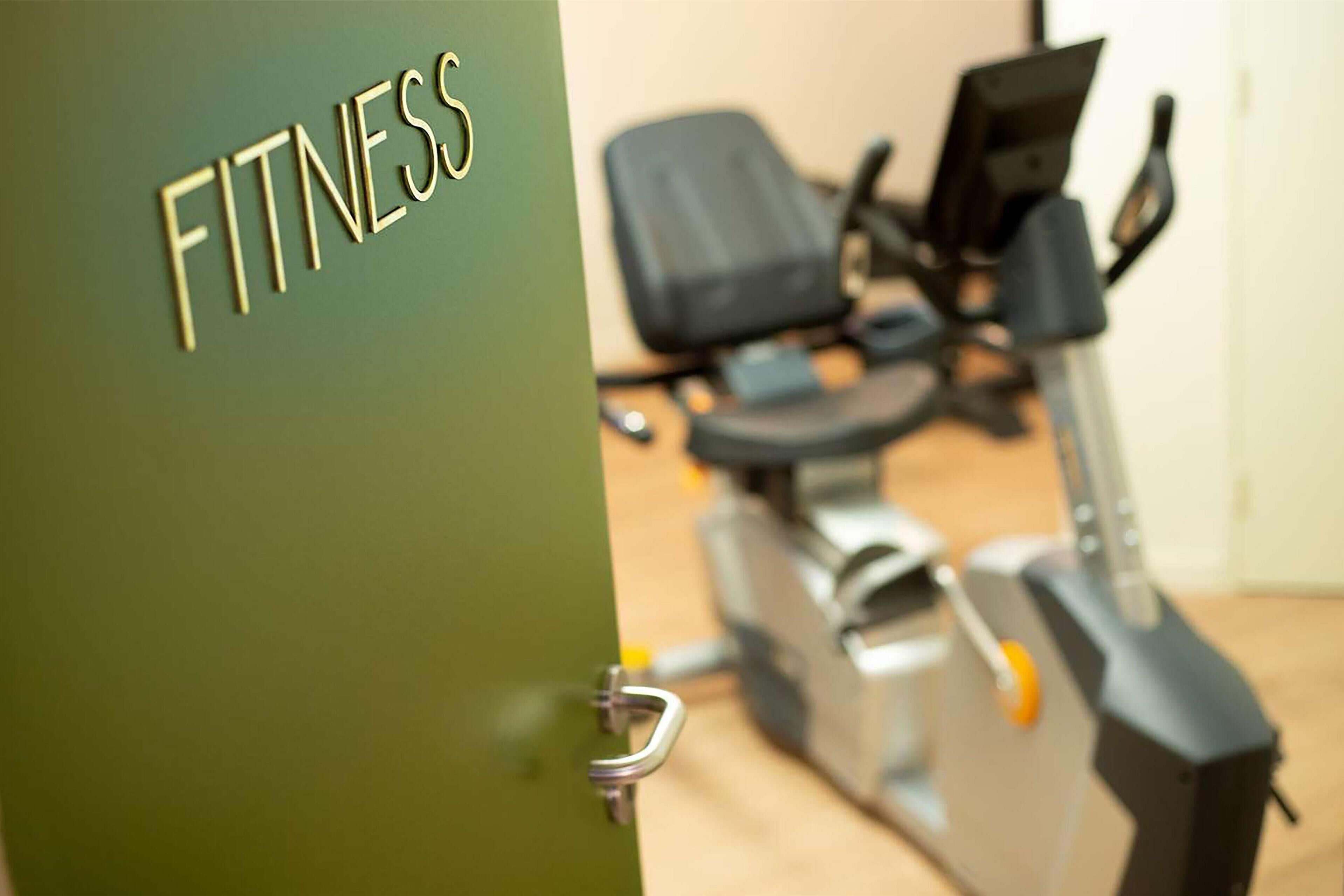 Een deur met de tekst 'FITNESS' die leidt naar een ruimte met fitnessapparatuur.