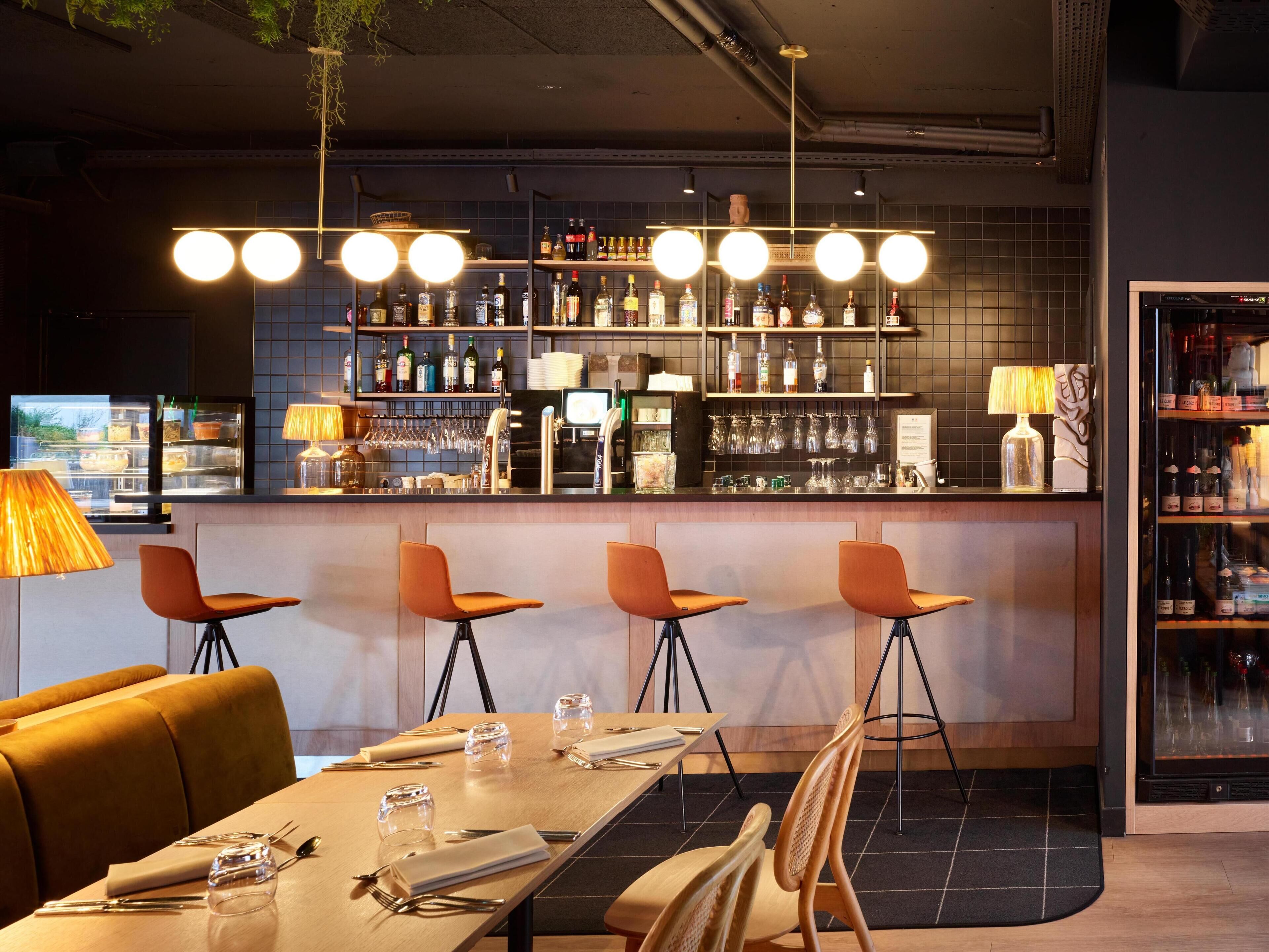 A bar area with a long counter, multiple stools, and a variety of bottles and glasses on shelves.