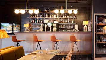 A bar area with a long counter, multiple stools, and a variety of bottles and glasses on shelves.
