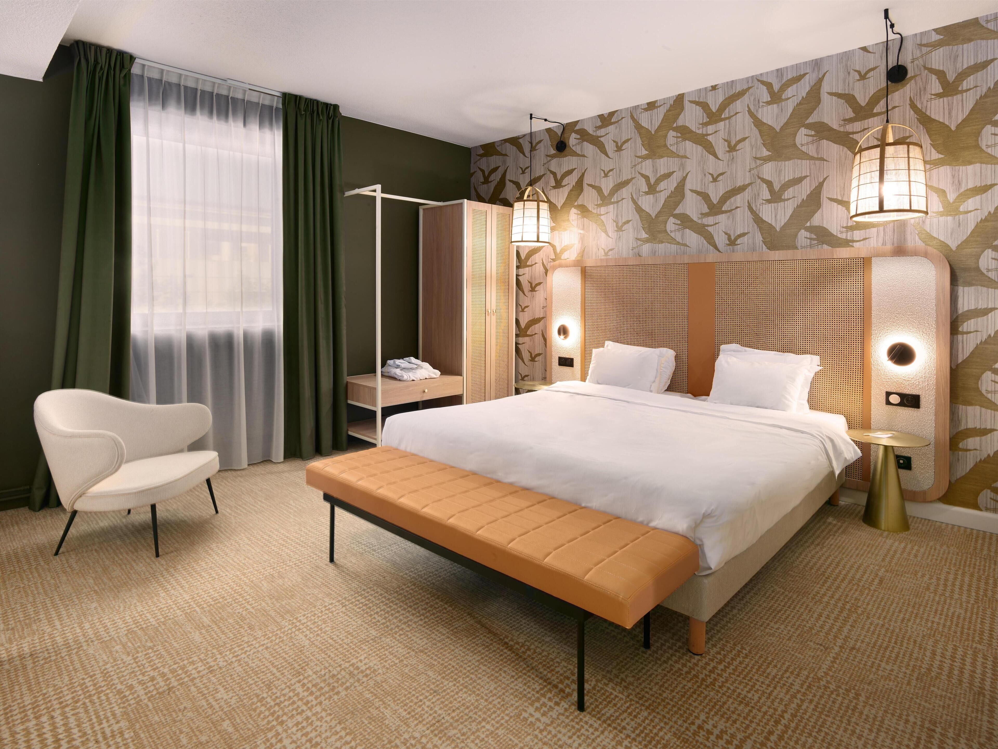 A hotel room with a bed, a bench, a chair, a wardrobe, and a nightstand.