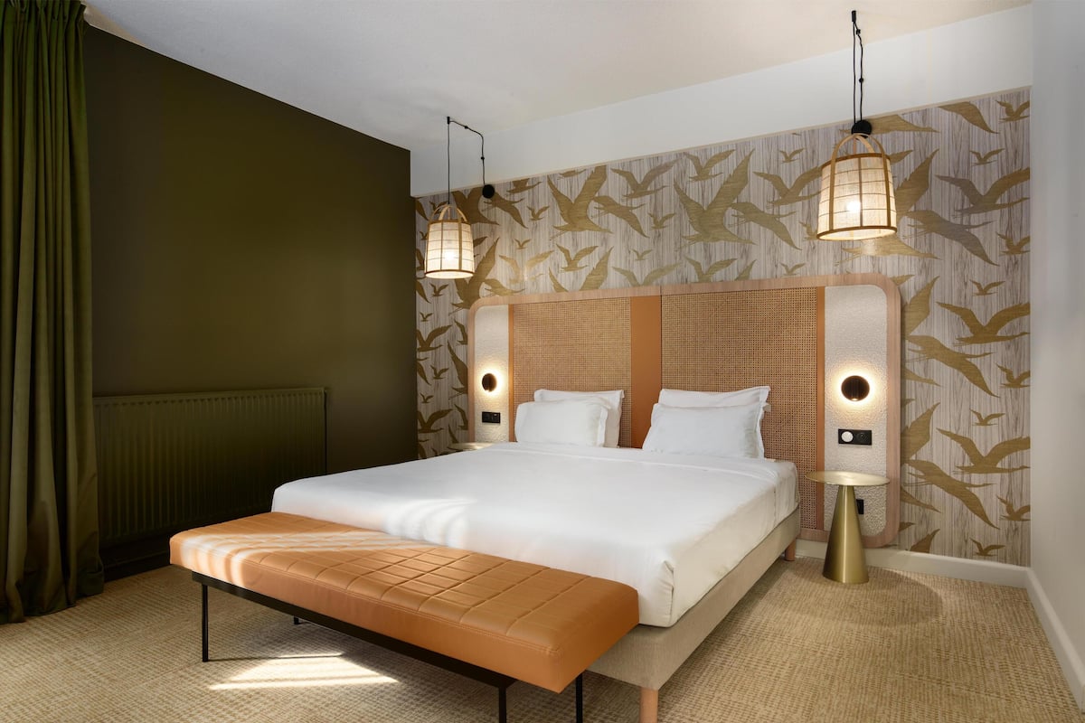 Una habitación de hotel con una cama grande, un banco, dos lámparas de pared y un papel tapiz estampado.