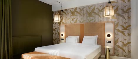 A hotel room with a large bed, a bench, two wall-mounted lamps, and a patterned wallpaper.