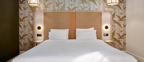 A hotel room with a large bed, two wall-mounted lamps, and a patterned wallpaper with bird designs.