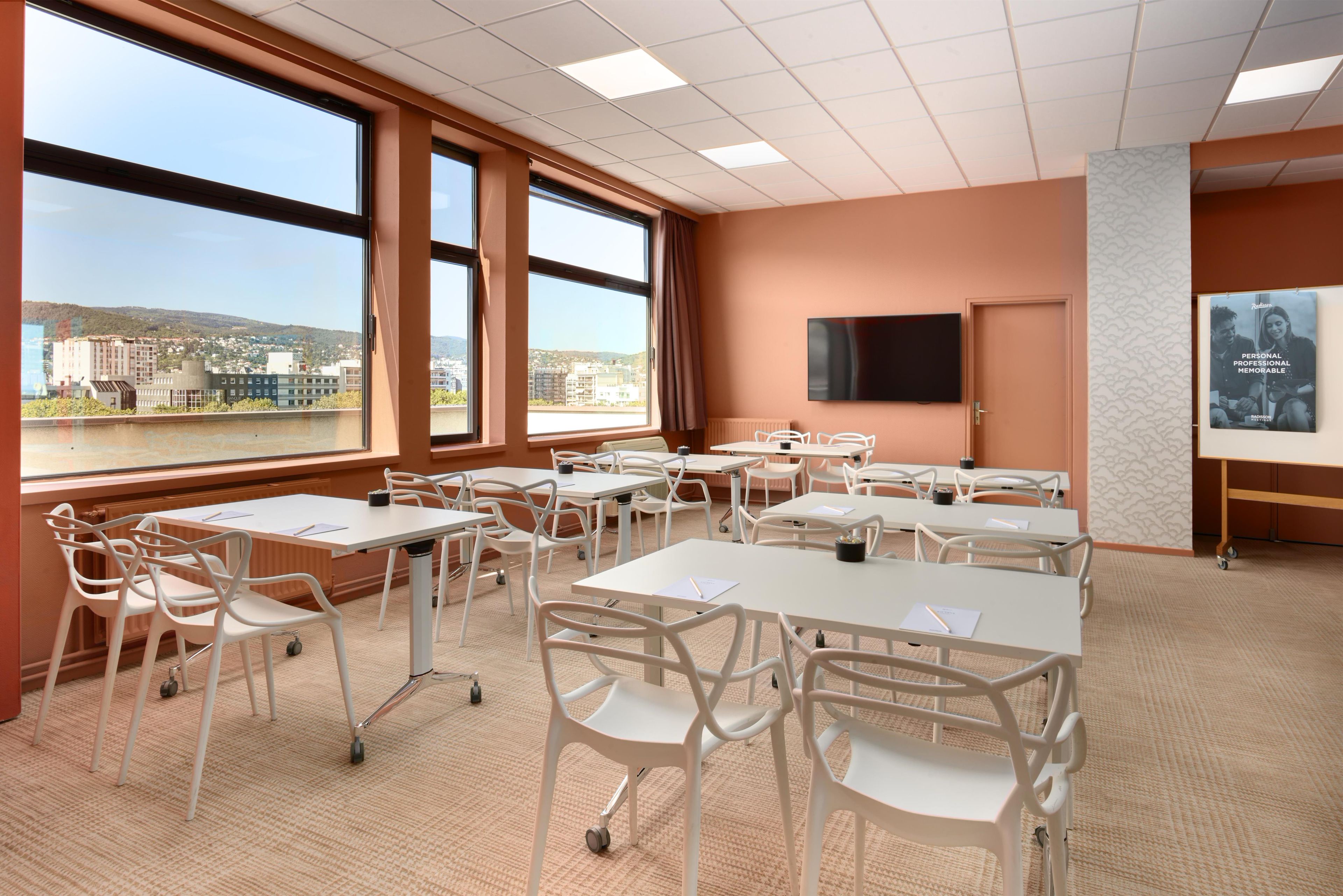 A conference room with large windows, white tables, and chairs.