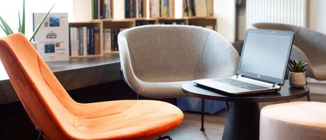 Un espace de lecture moderne avec un ordinateur portable sur une table, une bibliothèque et des sièges confortables.
