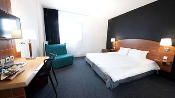 Une chambre d’hôtel avec un lit, un bureau et une chaise, une télévision et une fenêtre avec des rideaux.