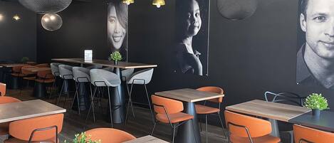A restaurant interior with tables, chairs, hanging pendant lights, and wall art.