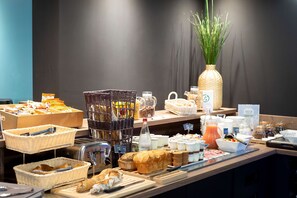 Un bufé de desayuno con diversos alimentos, cestas y una botella de jugo.