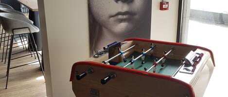 A foosball table in a room with a large poster on the wall, wooden flooring, and a window with a view of the street.