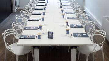Un salón de conferencias con mesas y sillas blancas, tarjetas de identificación y carpetas azules.