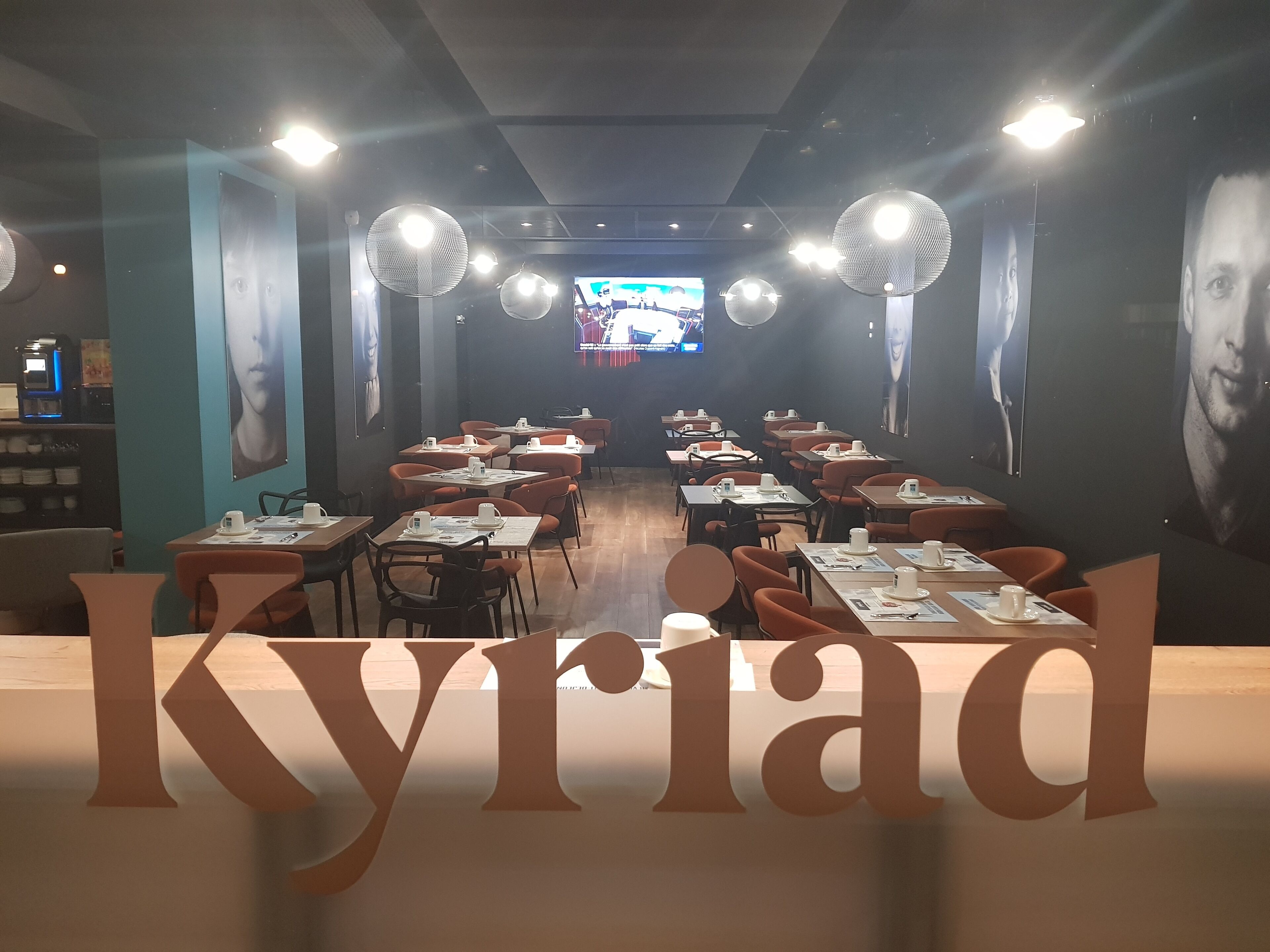 Un restaurante con mesas, sillas, una pantalla de televisión y carteles en las paredes.