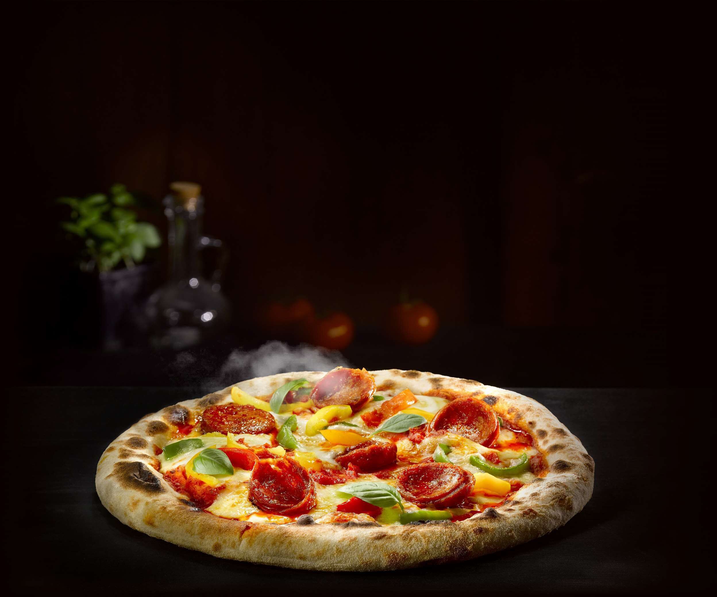 A pizza with pepperoni and vegetables on a dark surface.